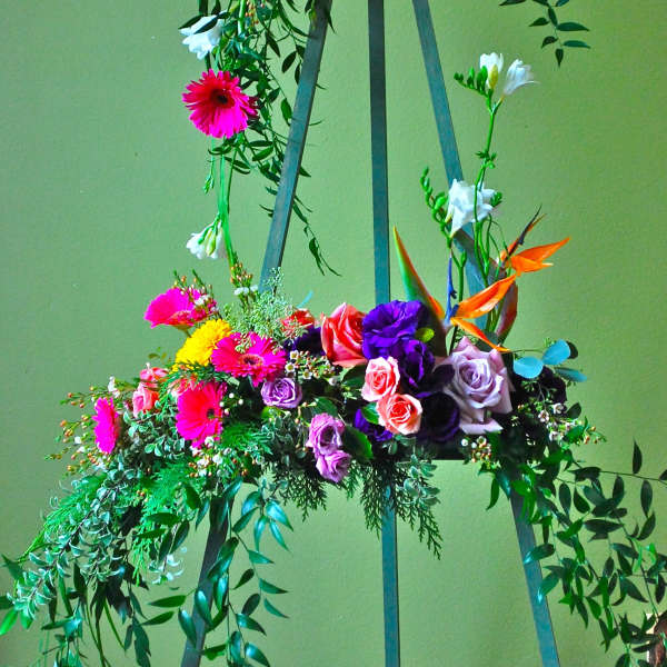 Tall floral arrangement on a metal stand with bright mixed blooms and trailing greenery