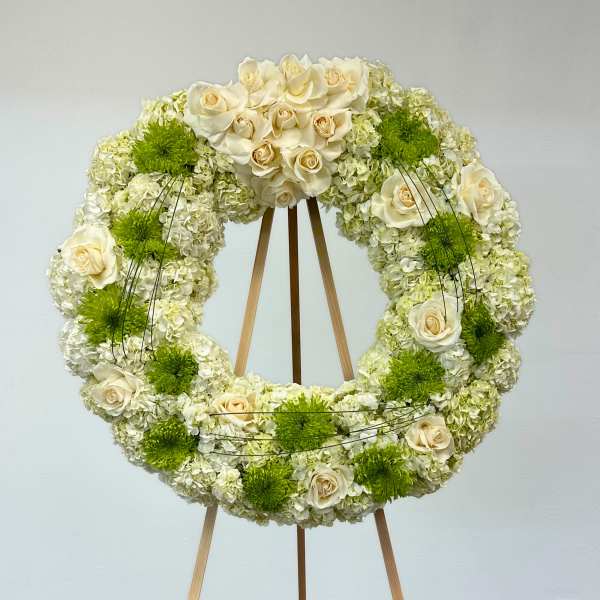 Circular floral wreath of white roses and green mums on a wooden easel