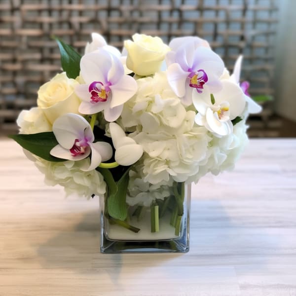White hydrangeas and pale orchids in a square glass vase