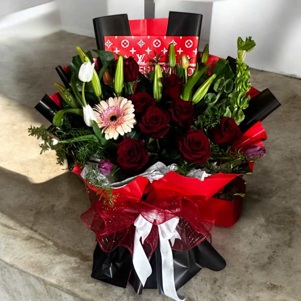Bouquet of red roses, lilies, and a pink gerbera daisy in red and black wrap