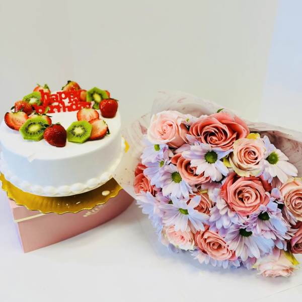 Birthday cake with fruit topping beside a pink rose and daisy bouquet