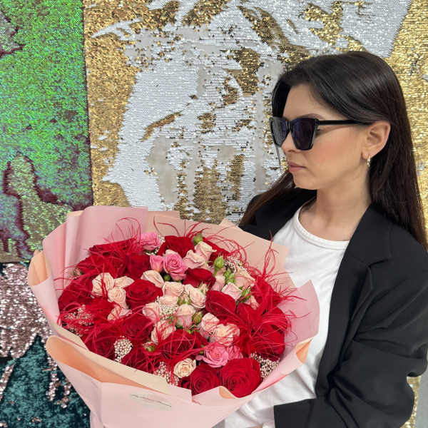 Woman holding a large bouquet of red and pink roses wrapped in pale pink paper
