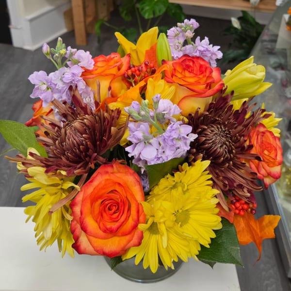 Bouquet of orange roses, yellow daisies, and lavender flowers in a glass vase