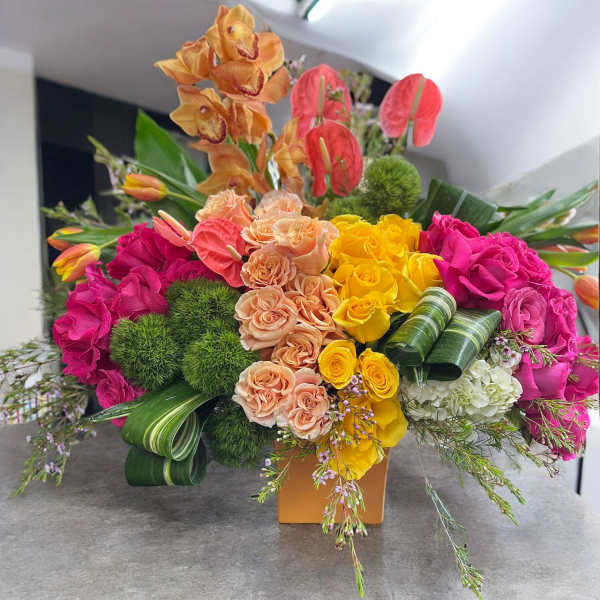 Bright mixed bouquet with roses, orchids, and anthuriums in a square vase