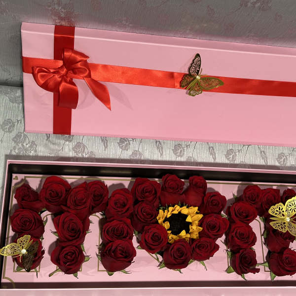 Pink gift box with red roses arranged inside and a red ribbon on the lid