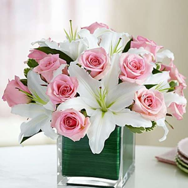 Pink roses and white lilies arranged in a clear square vase