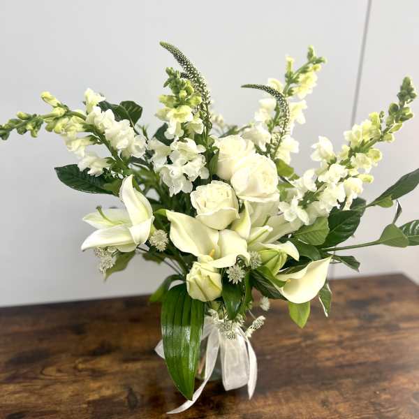 White floral arrangement with roses, calla lilies, and snapdragons in a clear vase