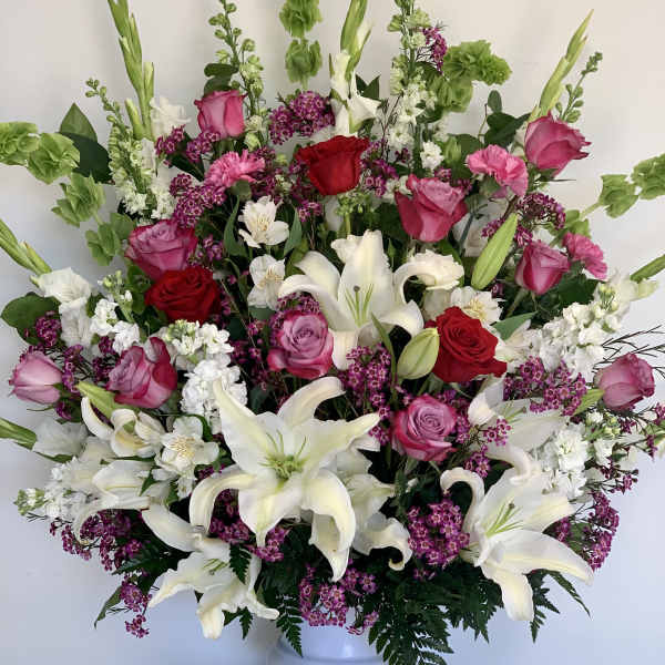 Large bouquet of white lilies, pink and red roses, and purple filler flowers in a white vase