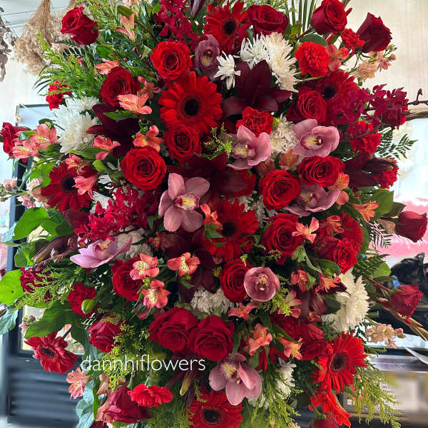 Large red floral standing spray with roses, gerberas, orchids, and white mums