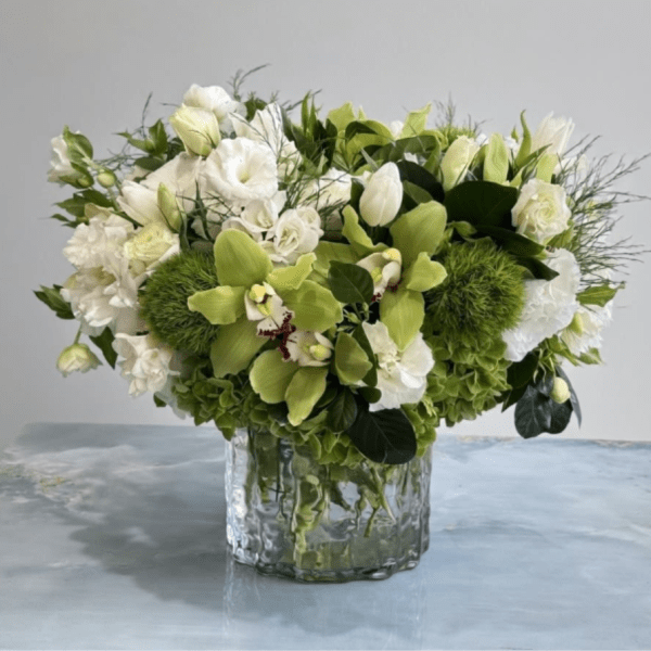 Low arrangement of white blooms and green orchids in a clear glass vase