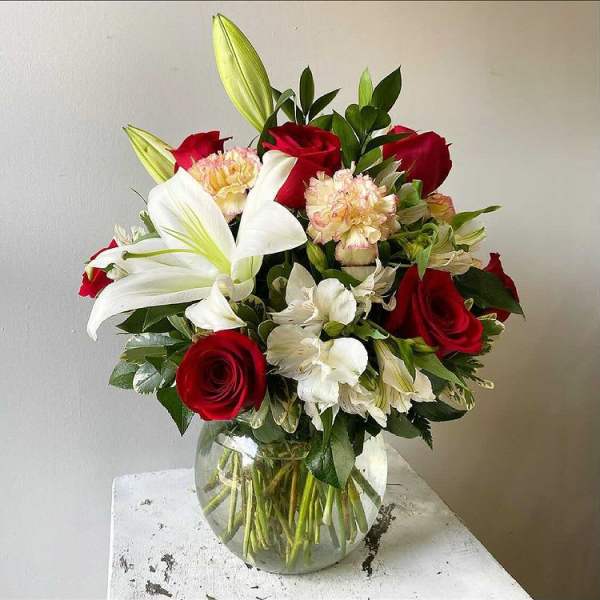 Bouquet of red roses, white lilies, and pale carnations in a glass vase