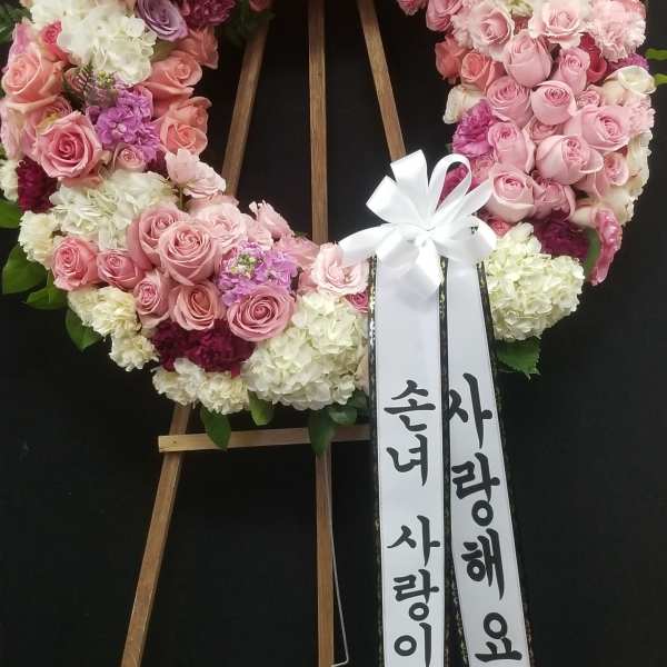 Pink and white floral wreath on a wooden stand with ribbon streamers