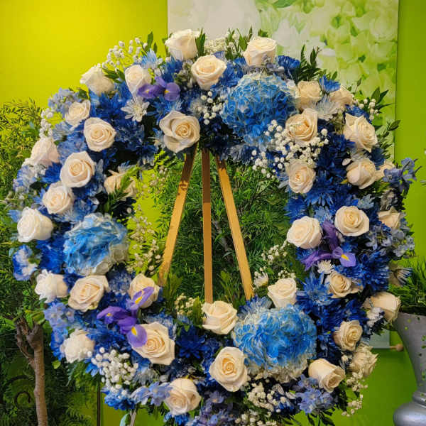 Large heart-shaped floral wreath with white roses and blue flowers on an easel