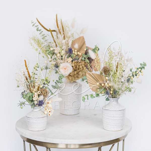 Three dried floral arrangements in white vases on a round table