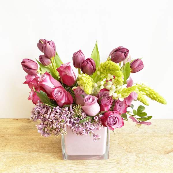 Pink and purple tulips and roses in a square glass vase