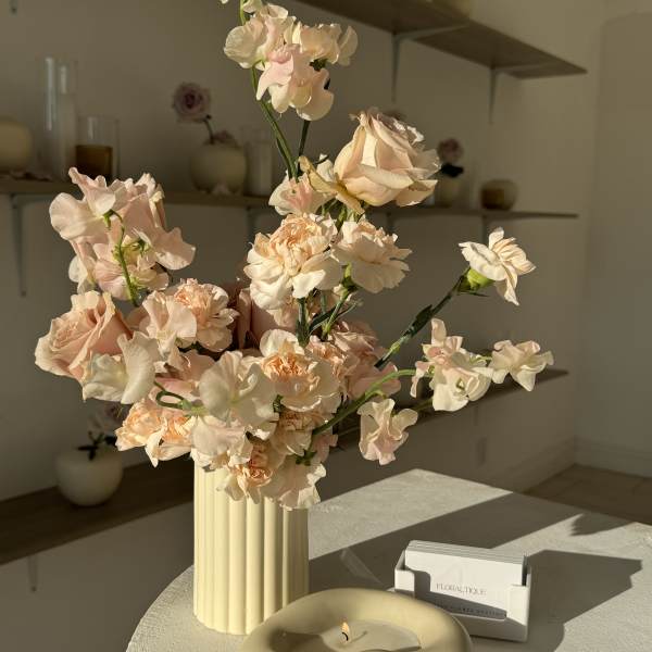 Blush and cream flowers in a ribbed vase beside a candle and card holder