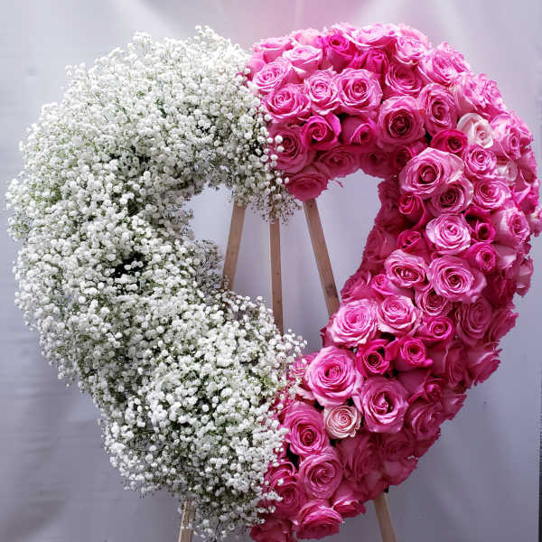 Heart-shaped floral wreath with pink roses and white baby's breath on a stand