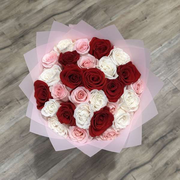 Bouquet of red, pink, and white roses wrapped in pale pink paper