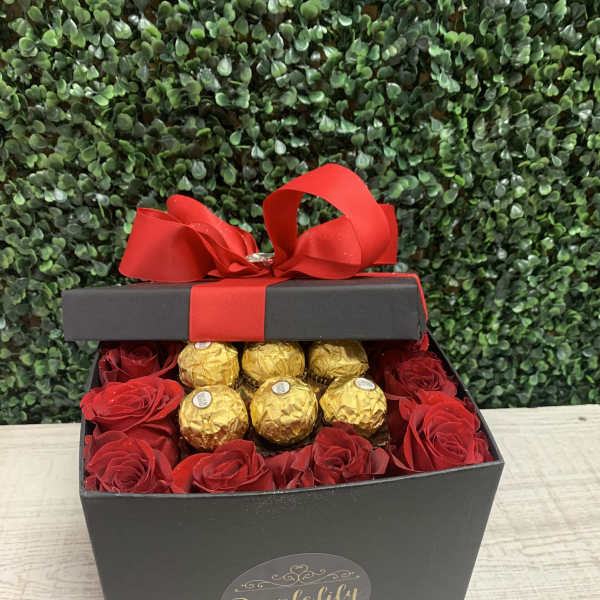 Black gift box with red roses and gold-wrapped chocolates topped by a red bow