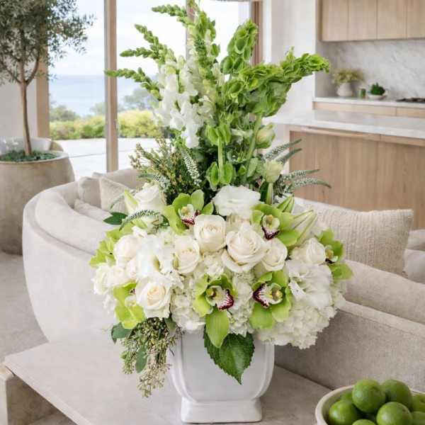 White and green floral arrangement in a white vase on a table