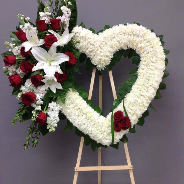 Heart-shaped floral wreath with red roses and white lilies on an easel