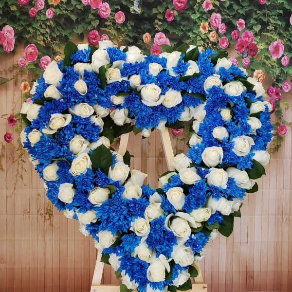 Heart-shaped floral wreath of white roses and blue chrysanthemums on an easel