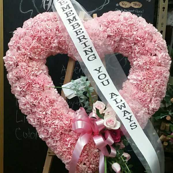 Pink heart-shaped floral wreath with a memorial ribbon on an easel