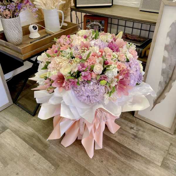 Large pastel bouquet of pink, white, and lavender flowers wrapped in white and pink paper