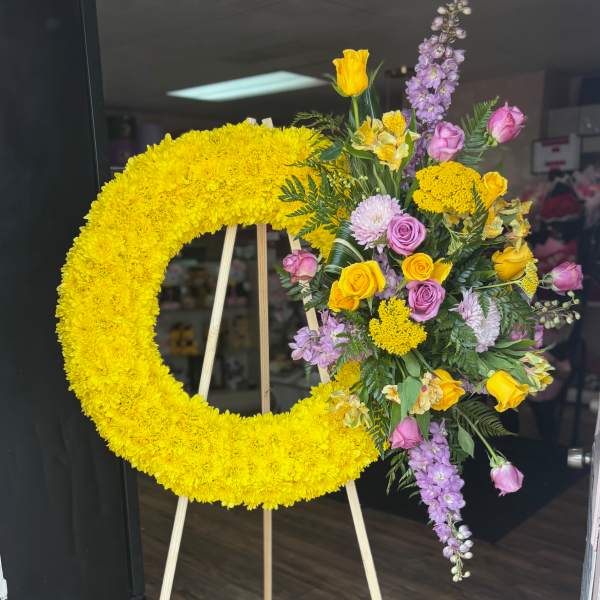 Yellow floral wreath on an easel beside a mixed bouquet