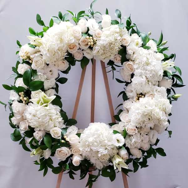 White floral wreath with roses and hydrangeas on a wooden stand