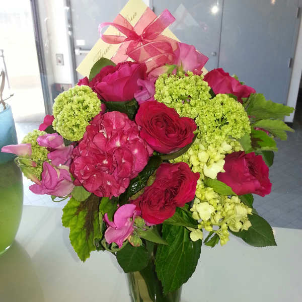 Pink and red flower bouquet in a clear glass vase with a ribbon
