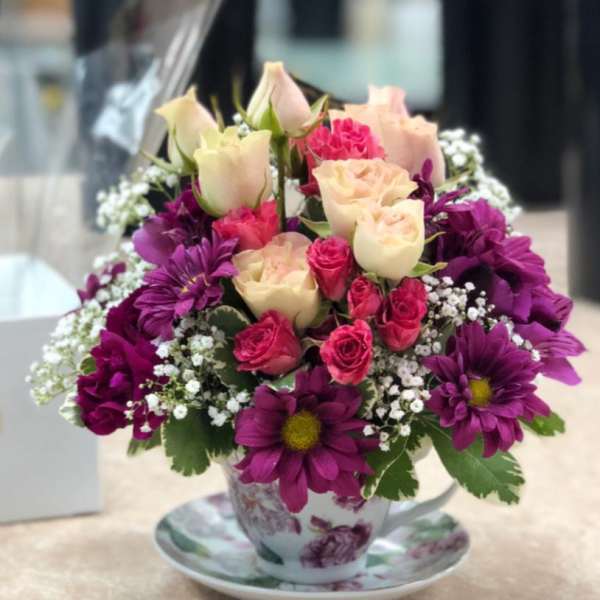 Bouquet of pink and cream roses with purple daisies in a floral teacup