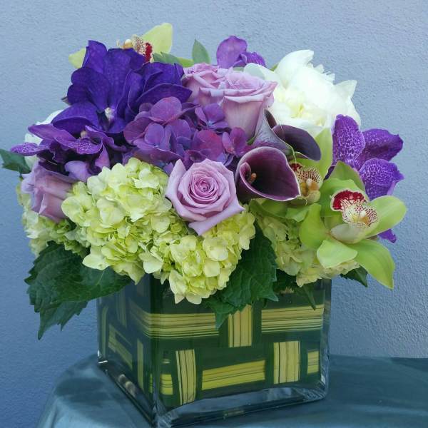 Purple and green floral arrangement in a square glass vase
