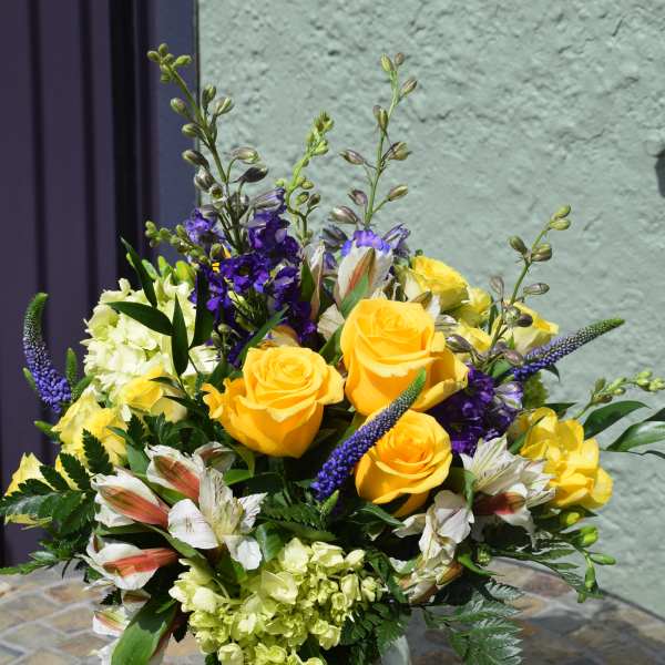 Yellow rose and purple flower arrangement with white blooms in a clear glass vase on a mosaic table