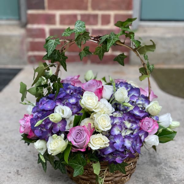 Basket arrangement of purple hydrangeas and pink and white roses with ivy arch
