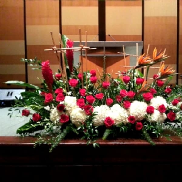 Large altar arrangement of red roses, white mums, and orange tropical flowers with wooden cross accents