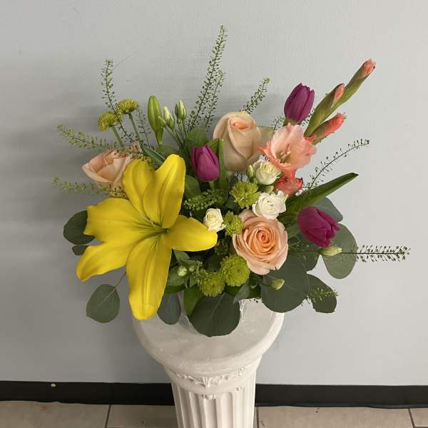 Mixed bouquet of yellow lilies, pink roses, and purple tulips in a white vase