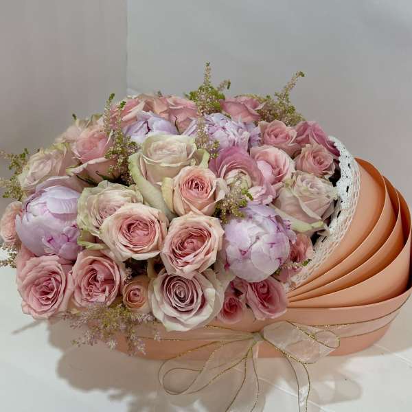 Bouquet of pale pink roses and peonies in a peach hatbox