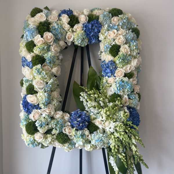 Square floral wreath on an easel with white roses, blue hydrangeas, and green accents