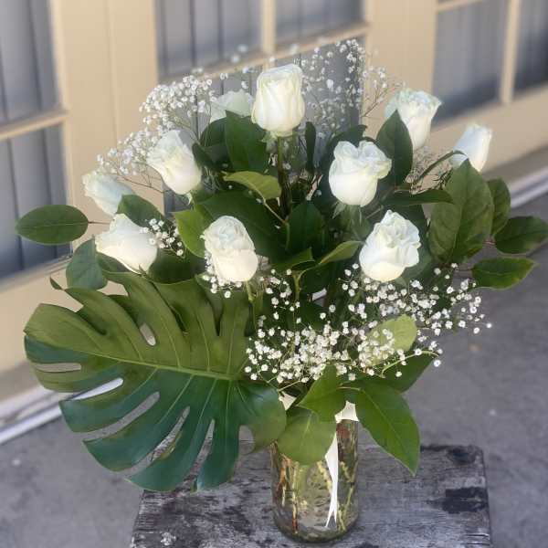 White roses in a glass vase with baby's breath and large tropical leaves