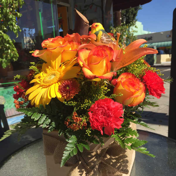 Orange and yellow floral arrangement in a burlap-tied box with a bird decoration