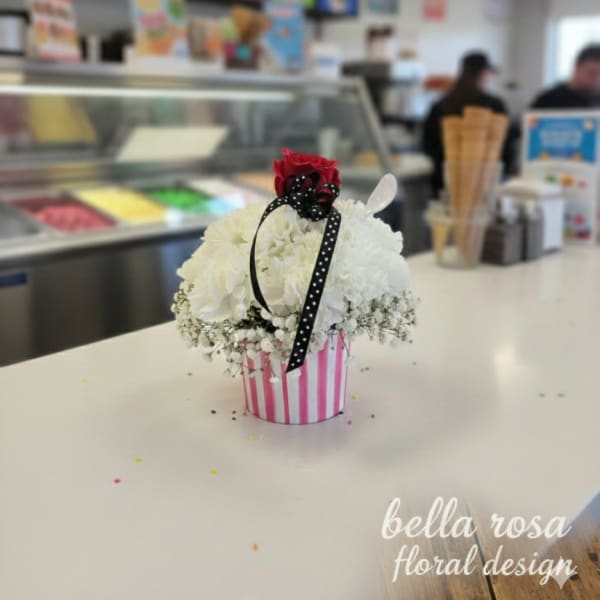 White floral arrangement in a pink striped container with a red rose topper