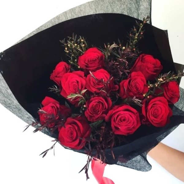 Bouquet of red roses wrapped in black paper with a pink ribbon