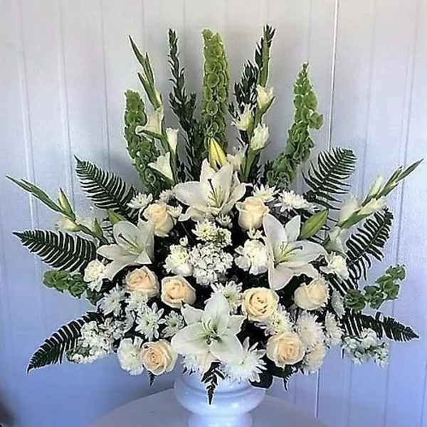 White floral arrangement in a white urn with lilies and roses
