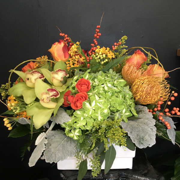 Mixed floral arrangement with orchids, roses, and hydrangea in a white container