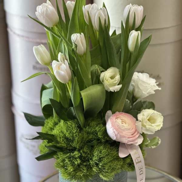 White tulips and pale pink blooms in a gray hatbox with green moss