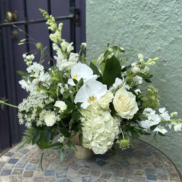 Low white arrangement with roses, orchids, hydrangeas, and snapdragons in a gold vase