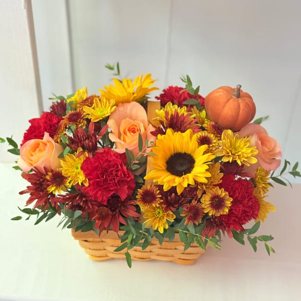Basket of mixed flowers with roses, sunflowers, and a small pumpkin