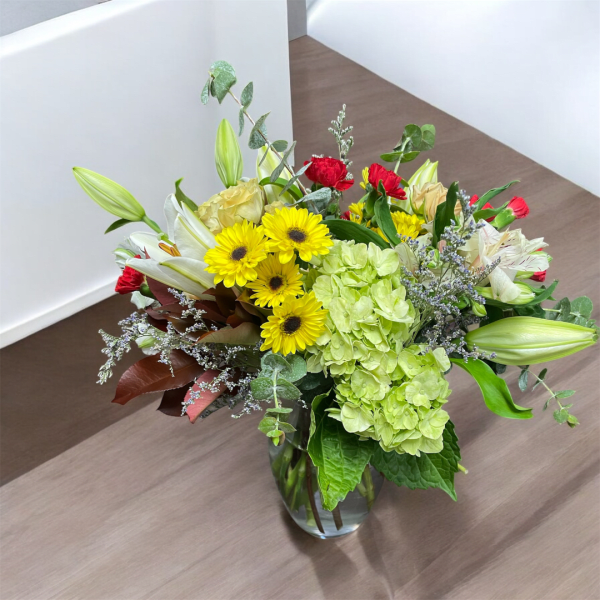 Mixed bouquet in a clear glass vase with yellow daisies and lilies