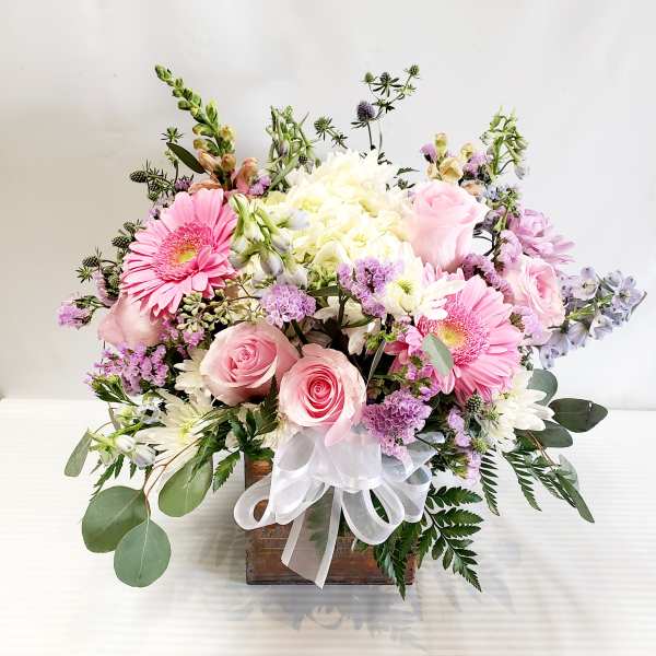 Pink roses and gerbera daisies in a wooden box with a white ribbon